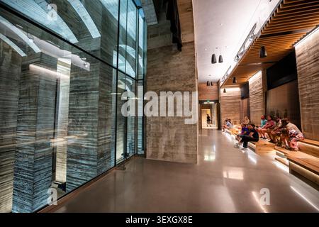 Intérieur du musée de l'Undercroft du Lincoln Memorial à Washington DC | WASHINGTON D.C., États-Unis — Les visiteurs assis sur des gradins en bois dans le musée nouvellement ouvert de l'Undercroft du Lincoln Memorial regardent à travers un mur de verre de toute hauteur dans la chambre de fondation en béton brut en dessous. Le vide existe parce que la construction de 1914 de l'architecte Henry Bacon a nécessité 122 pieux en tuyau d'acier enfouis jusqu'au substrat rocheux à environ 50 pieds (15 m) sous la plaine plates-forme de Potomac récupérée, laissant un espace caverneux sous le sol en marbre qui est resté largement inutilisé pendant un siècle avant sa réouverture le 25 juin 2026 sur environ 15 000 pieds carrés (1,39 Banque D'Images
