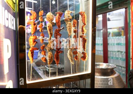 Poulet fraîchement grillé, poulet tikka et barbecue de style tandoori présentés sur des brochettes métalliques dans une vitrine de restaurant le soir. Banque D'Images
