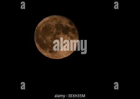 La pleine lune dorée de fraise brille brillamment dans un ciel nocturne noir clair pendant juin en Grèce. Astrophotographie minimaliste avec espace de copie. Banque D'Images