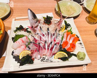 Gros plan d'une assiette de sashimi magnifiquement arrangée avec des tranches de poisson cru frais, du citron, du wasabi et des algues dans un restaurant japonais. Banque D'Images