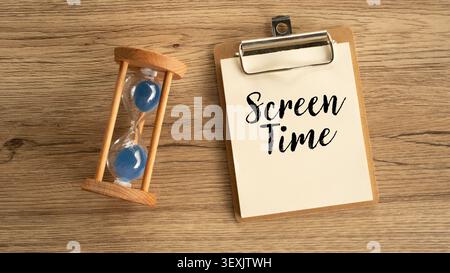 Vue plate du presse-papiers de bureau avec le temps d'écran de texte manuscrit placé à côté du concept de minuterie de sablier en bois de détox numérique et de limite Banque D'Images