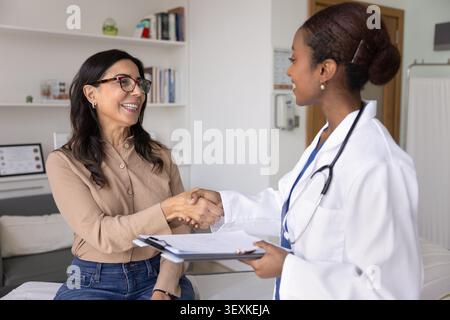 Femme patiente joyeuse donnant une poignée de main à un jeune médecin africain confiant Banque D'Images