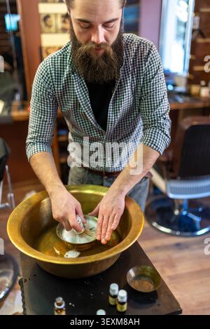 Barbier préparant une mousse à raser riche dans un bol de bassin traditionnel en laiton Banque D'Images