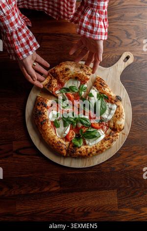 Une jeune femme prend une tranche de pizza fraîchement cuite. Isolé. Éclairage de studio professionnel. Banque D'Images