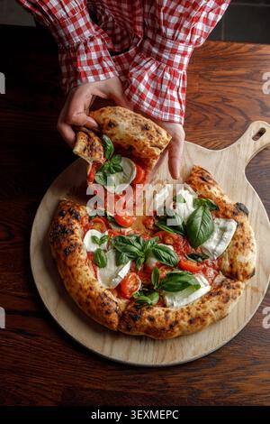 Une jeune femme prend une tranche de pizza fraîchement cuite. Isolé. Éclairage de studio professionnel. Banque D'Images