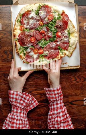 Une jeune femme prend une tranche de pizza fraîchement cuite. Isolé. Éclairage de studio professionnel. Banque D'Images