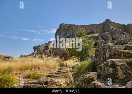 Ancien mur de château en pierre entouré de grands rochers et d'une végétation sauvage sous un ciel bleu clair. Banque D'Images