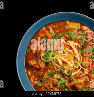 Bol de soupe traditionnelle hongroise au goulash avec du bœuf, des légumes et des pâtes sur fond noir Banque D'Images