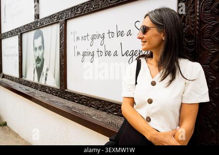 Zanzibar, Tanzanie - 15 octobre 2025 : femme adulte moyenne souriant à côté du panneau d'affichage de l'entrée du musée Freddie Mercury dans Stone Town Zanzibar, musique l Banque D'Images