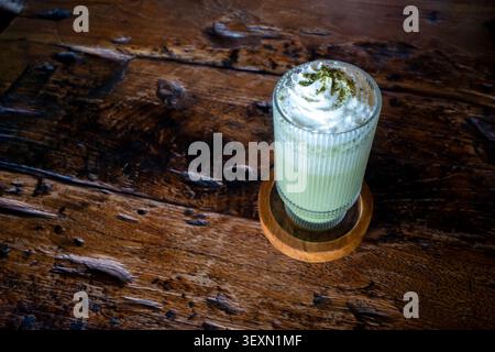 Un verre de milkshake Matcha Green Tea nappé et garni d'un biscuit et de pâtes blanches. Banque D'Images