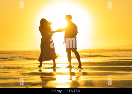Couple aime une promenade au coucher du soleil le long de la plage tout en se tenant la main et en jouant dans le sable à un endroit côtier Banque D'Images