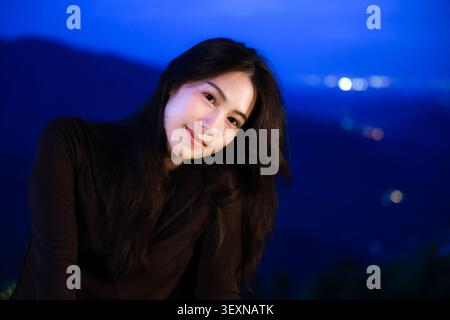 Une jeune femme à cheveux longs chemise noire souriante en plein air nuit bleu montagne fond serein beauté naturelle paisible lumière douce détendue pose bonheur Banque D'Images