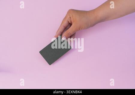 Main féminine tenant une carte en plastique noire sur un fond rose. Banque D'Images