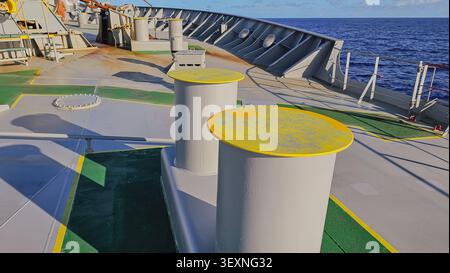 Gros plan horizontal de bittes d'amarrage marines robustes avec des sommets jaunes sur un pont de navire, utilisées pour sécuriser les lignes d'amarrage avec un océan bleu profond dedans Banque D'Images