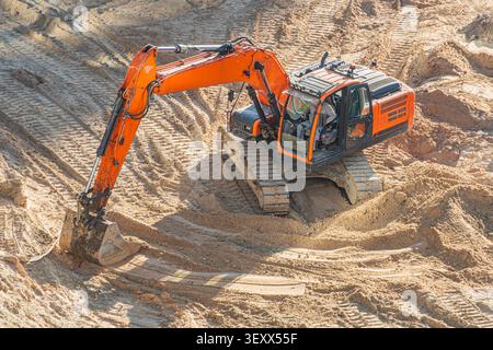 Grande pelle orange travaillant sur terrain sablonneux, bras articulé et godet creusant, conducteur concentré dans la cabine ouverte, chaînes extra-robustes quittant Dee Banque D'Images