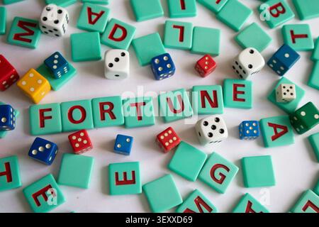 Des carreaux de lettres et des dés colorés de différentes tailles sont dispersés sur une table. Le mot FORTUNE peut être épelé en utilisant certaines des tuiles. Image conceptuelle Banque D'Images