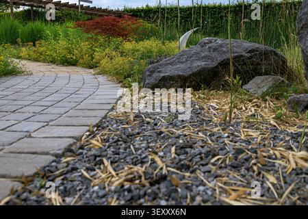 Vue rapprochée à faible angle d'un chemin de jardin pavé de pierre qui serpente devant de gros rochers, un revêtement de sol en gravier et un érable japonais rouge. Banque D'Images