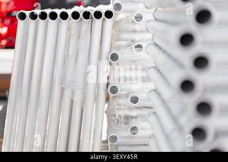 Tuyaux industriels blancs en pvc ou en métal soigneusement empilés et enveloppés dans un film plastique de protection dans un entrepôt de fabrication de construction Banque D'Images