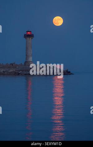 Pleine lune de fraise se levant derrière le phare de Trakata près d'Euxinograd à Varna Bulgarie Banque D'Images