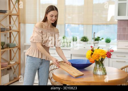 Heureuse jeune femme avec planche à découper propre à la table en bois dans la cuisine Banque D'Images
