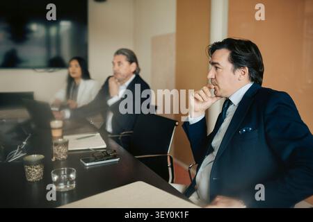 Professionnel d'affaires masculin concentré assis avec la main sur le menton dans la réunion au bureau Banque D'Images