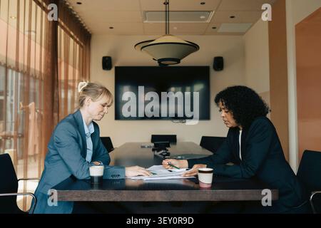 Diverses femmes d'affaires examinant des documents tout en s'asseyant autour de la table dans le bureau Banque D'Images