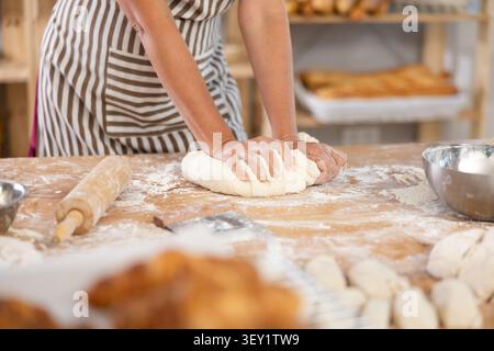 Pâtes mignonnes disposées sur la table dans la boulangerie avec un gros plan des mains féminines pétrissant habilement la pâte à la chaîne de production alimentaire Banque D'Images