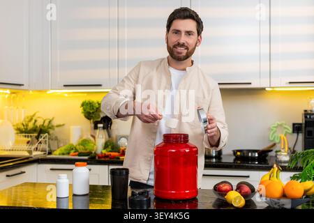 L'homme d'âge moyen ajoute de la poudre de protéine dans le shaker avec du lait souriant pour l'entraînement de fitness dans la cuisine à la maison. Young Guy secoue la bouteille pour une alimentation saine nutrit Banque D'Images