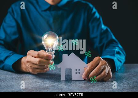 L'idée d'innovation immobilière créative montre des économies d'énergie d'ampoule de maison, l'homme d'affaires tient ampoule incandescente près du modèle de maison de papier pour prêt hypothécaire pro Banque D'Images
