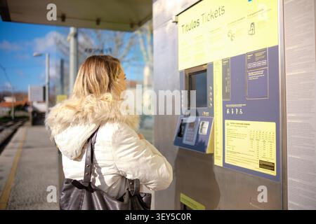 Femme utilisant un distributeur automatique de billets dans une station de transport public par une journée ensoleillée Banque D'Images
