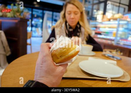 Personne tenant un krapfen avec du sucre en poudre tout en dînant dans un café de boulangerie Banque D'Images