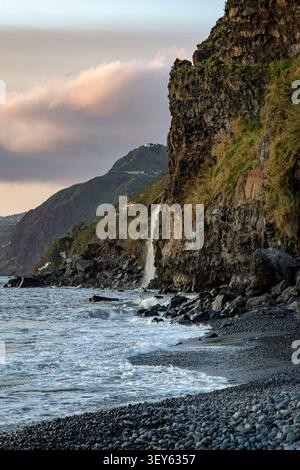 Une cascade côtière descend en cascade des falaises volcaniques escarpées dans l'océan Atlantique à Ponta do sol, Madère, Portugal. Paysage marin spectaculaire avec noir Banque D'Images