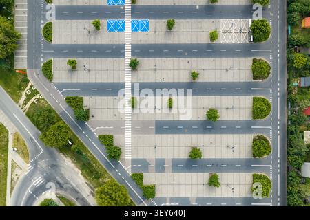 Vue aérienne d'un parking vide avec des places de stationnement marquées, des places de stationnement accessibles et des arbres verts entourant la zone pavée à Warszawa, Woje Banque D'Images