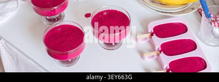 Mélanger les fraises, les bananes, les betteraves et le yogourt grec dans un mélangeur pour créer de la crème glacée. Les bols et les moules à glaçons reposent sur un comptoir de cuisine avec Banque D'Images