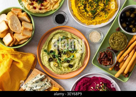 Une planche de charcuterie vibrante présente du brocoli, du curcuma, du houmous classique et de la betterave, associés à des olives, craquelins, et garnitures fraîches, parfait pour Banque D'Images