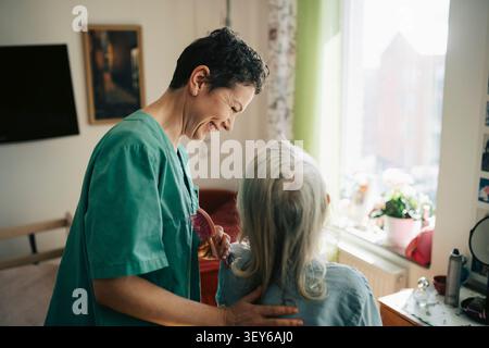 Vue de côté d'une infirmière heureuse prenant soin d'une femme âgée en maison de retraite Banque D'Images
