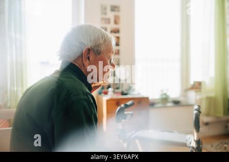 Homme aîné réfléchi portant des lunettes pendant qu'il était assis dans une maison de retraite Banque D'Images