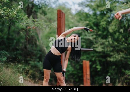 Jeune femme s'étirant à l'extérieur dans une tenue d'entraînement noire pendant une séance de fitness en plein air Banque D'Images