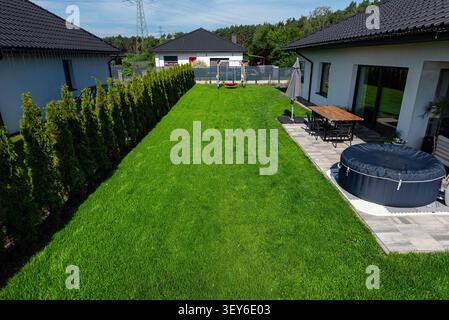 Arrière-cour d'une maison moderne avec une pelouse bien entretenue, clôture d'intimité, patio et bain à remous Banque D'Images