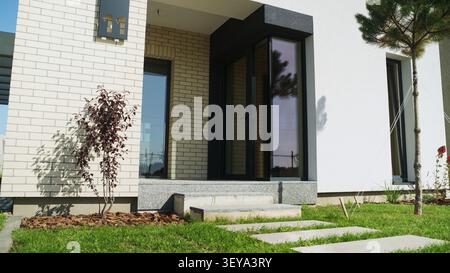 Entrée de maison moderne à l'architecture contemporaine, combinant murs blancs et briques, grandes fenêtres et jardin paysager Banque D'Images
