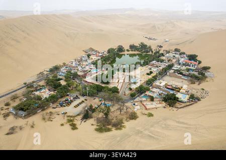 Vue aérienne de l'oasis de Huacachina entourée de vastes dunes de sable, de palmiers et de bâtiments à Huacachina, ICA, Pérou. Banque D'Images