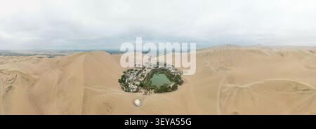 Vue aérienne de l'oasis de Huacachina entourée de vastes dunes de sable sous un ciel nuageux, Huacachina, ICA, Pérou. Banque D'Images