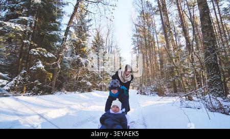 Famille faisant de la luge à travers les bois enneigés, partageant la joie hivernale et le moment de lier Banque D'Images