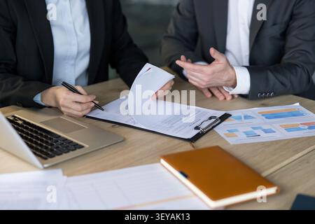 Professionnels des affaires examinant les termes de l'accord et discutant des détails financiers importants tout en signant un contrat d'entreprise important sur un bureau en bois avec un ordinateur portable et des documents Banque D'Images