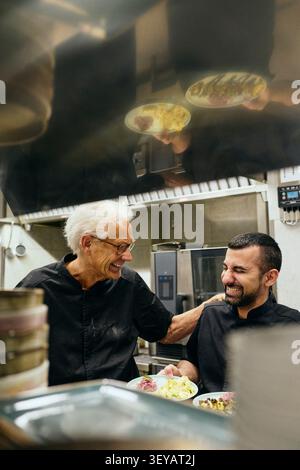 Deux chefs masculins riant tout en travaillant ensemble dans la cuisine commerciale Banque D'Images