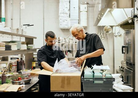 Deux chefs masculins ouvrant des boîtes de livraison dans la cuisine du restaurant Banque D'Images