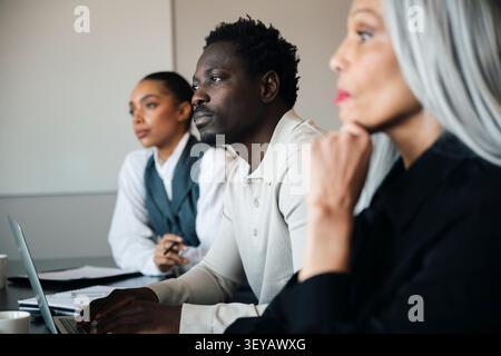 Groupe de collègues diversifiés regardant loin réfléchi pendant la présentation du bureau Banque D'Images