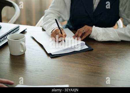 Milieu de section de femme d'affaires remplissant le formulaire tout en étant assis à table dans le bureau Banque D'Images