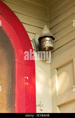 Une lumière de porche accentue le parement de shiplap vert et un cadre de porte rouge sur une vieille maison vacante. Banque D'Images