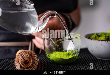 Gros plan d'Une femme versant de l'eau chaude dans le thé Matcha vert avec la main visible Banque D'Images